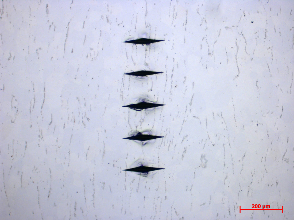 Titanium sample for metallurgical testing, with five knoop microhardness indentations.