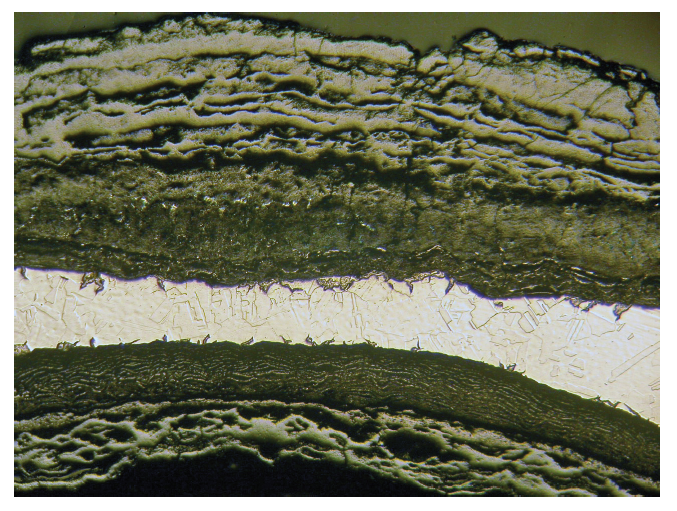 Optical micrograph of corroded steel pipe showing intergranular attack and reduced thickness 16X.